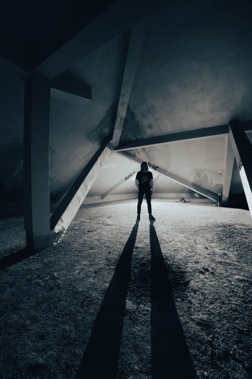 Free A person stands under an angular structure, casting a long shadow. Stock Photo