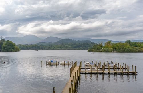 Free Tranquil lakeside scene with a pier, boats, and scenic mountain backdrop. Stock Photo