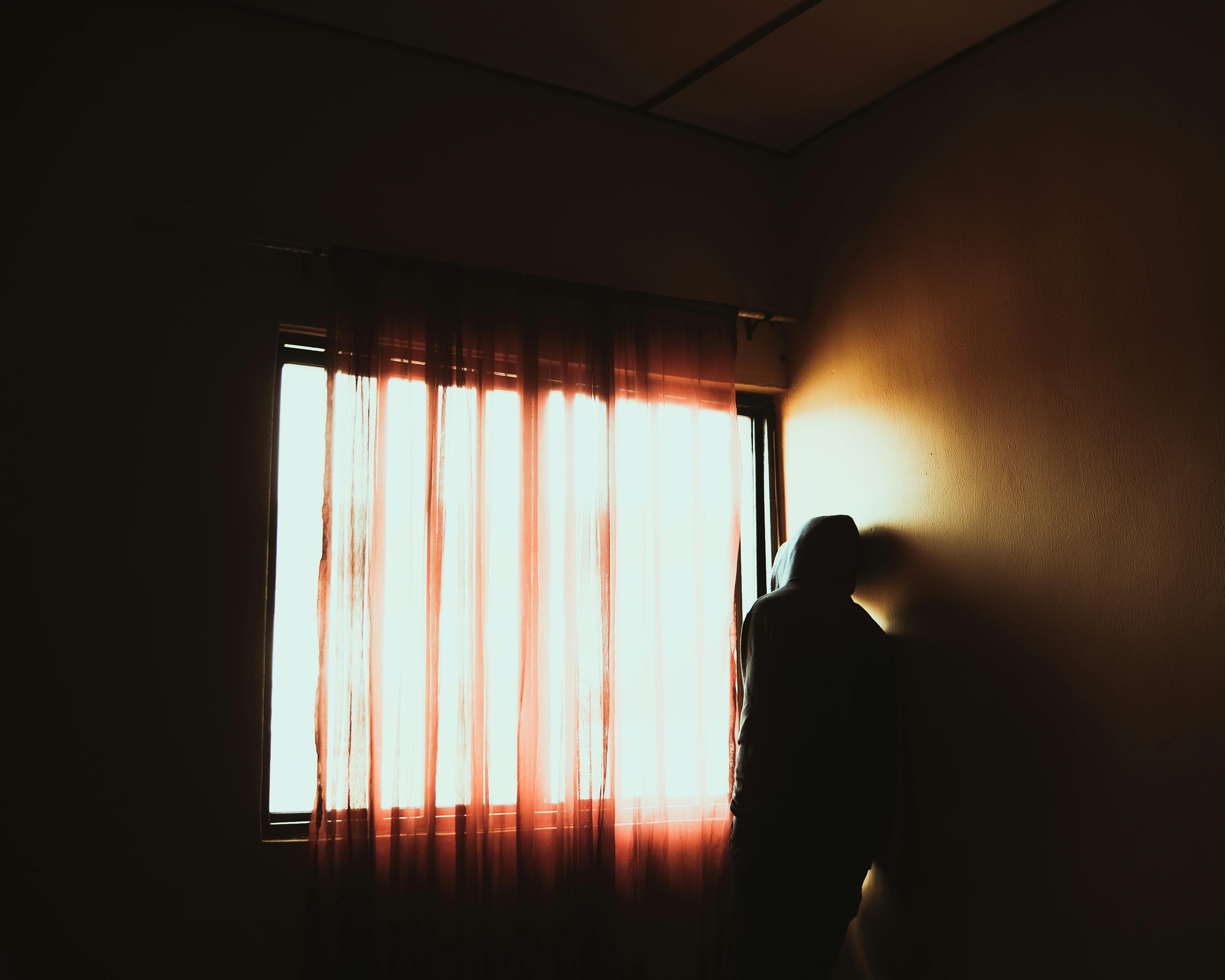 Free A solitary figure stands by a sunlit window, creating a dramatic silhouette. Stock Photo