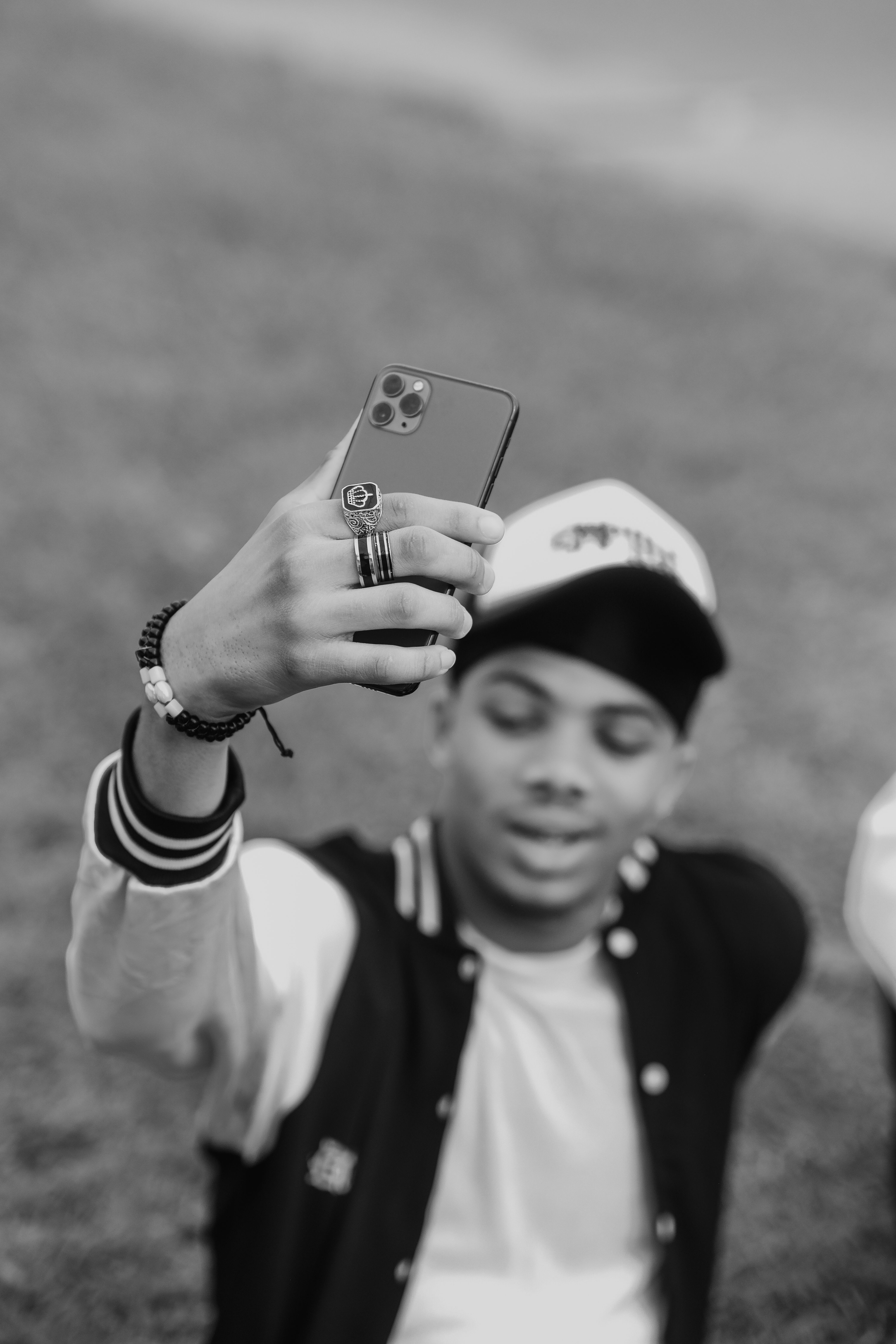 A teenager takes a selfie with a smartphone in a black and white themed image outdoors.