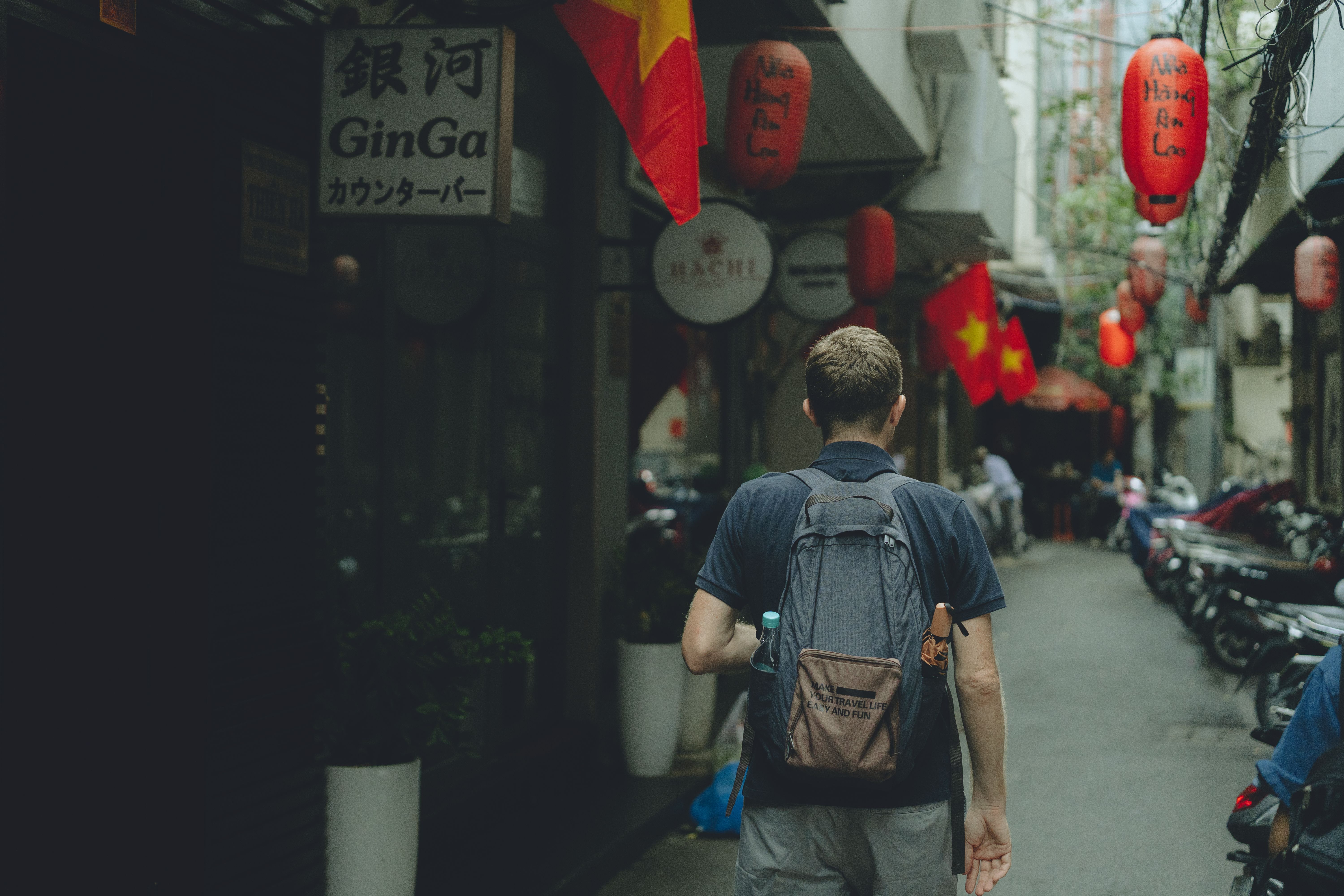 A man walks through a colorful alley in Ho Chi Minh City, Vietnam, adorned with Vietnamese flags and lanterns.