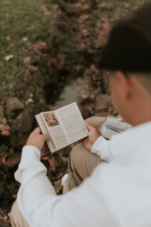 Free Young man sitting in a park while reading a book, enjoying a peaceful outdoor setting. Stock Photo