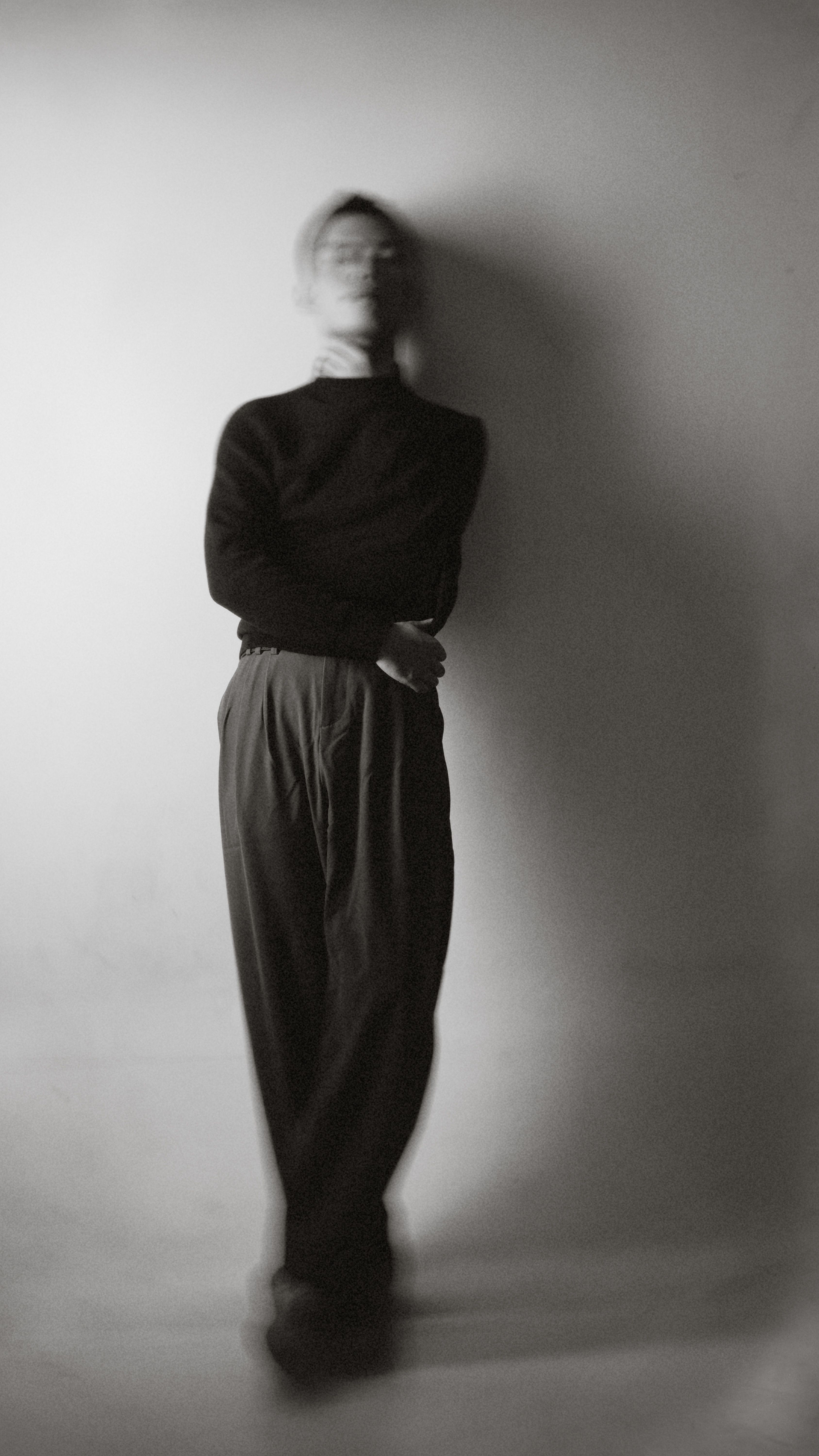 A man in a black shirt and pants leaning against a wall · Free Stock Photo