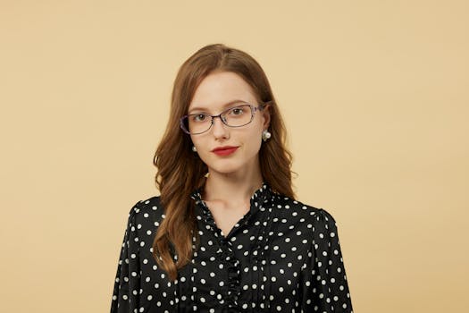 Elegant woman wearing glasses and a polka dot blouse posing against a soft backdrop.