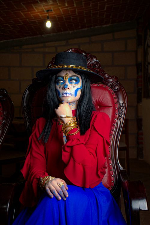 Free A woman in traditional costume and makeup for Day of the Dead, sitting elegantly indoors. Stock Photo