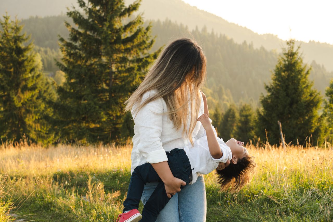 a mother and child share a joyful moment outdoors against a scenic mou