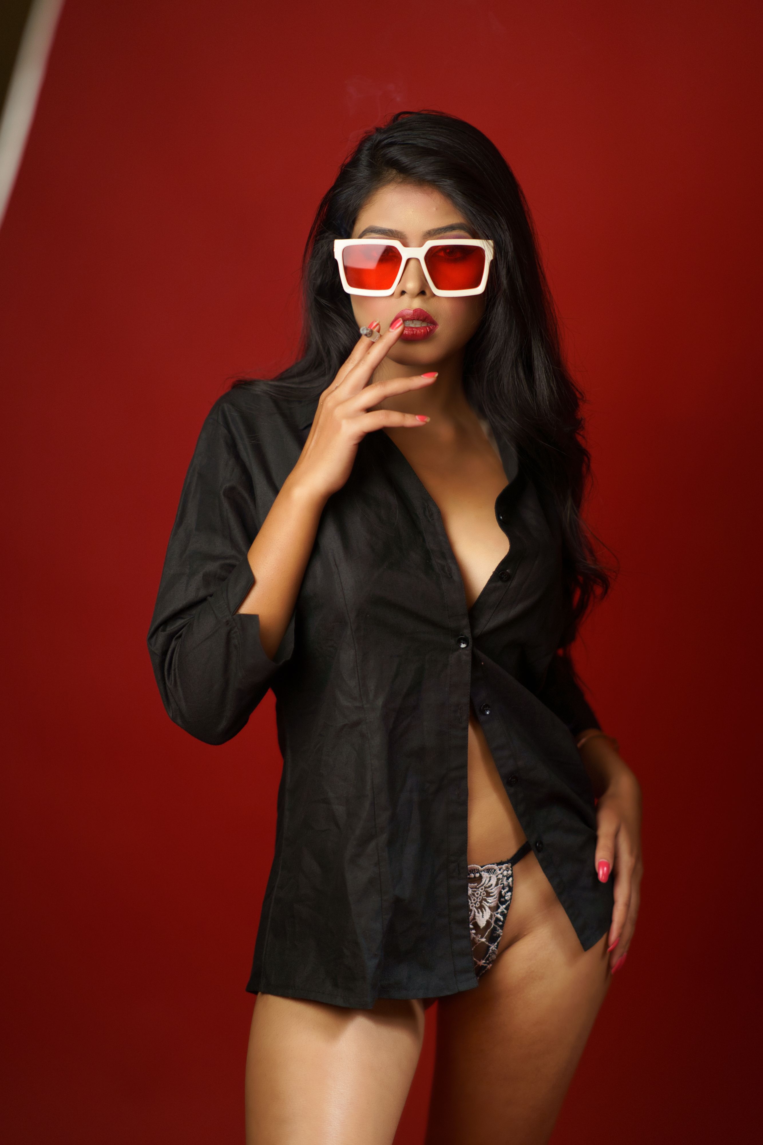 Fashion portrait of a young woman in sunglasses and black shirt against a red background.
