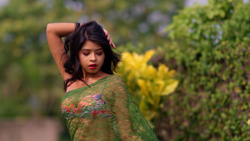 Portrait of a woman in a green dress, posing gracefully in a lush garden setting.