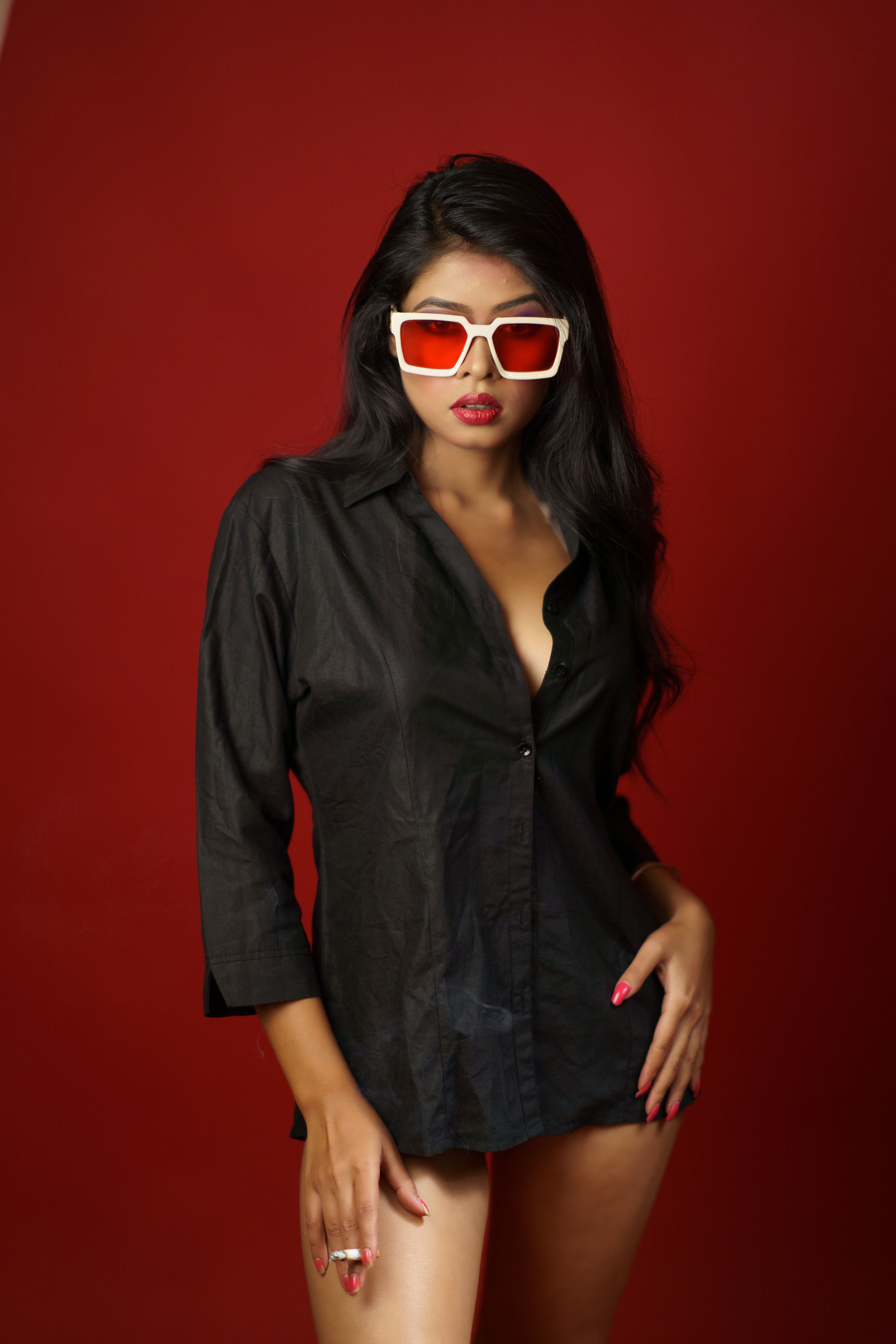 Elegant woman posing confidently indoors, wearing sunglasses and a chic black shirt.