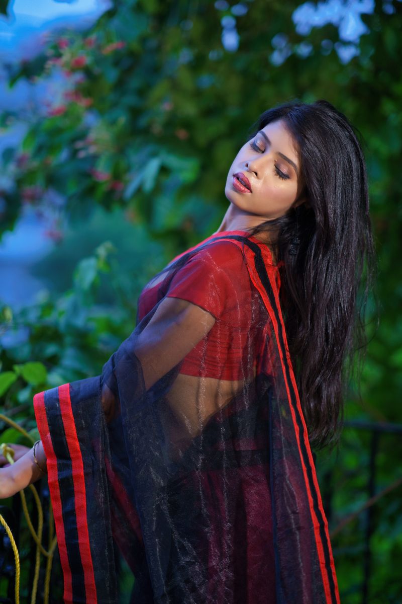 Beautiful woman in a traditional red sari poses gracefully outdoors with a serene expression.