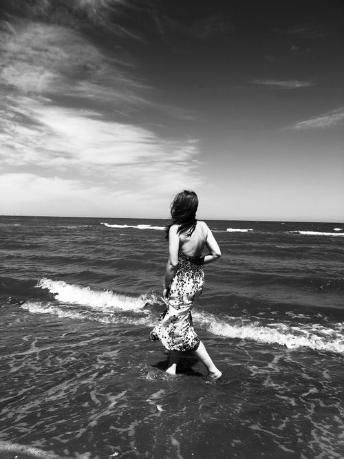 Free A woman walks along the beach in a flowing dress, captured in black and white. Stock Photo