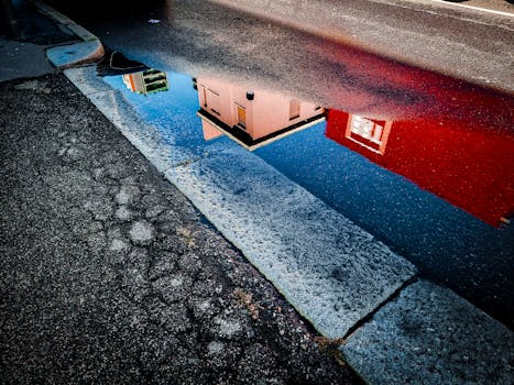 Colorful urban building reflection in a rain puddle on a textured street pavement.