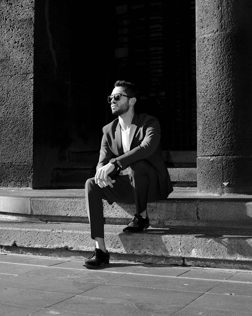 Free Black and white portrait of a stylish man sitting on city steps, exuding urban sophistication. Stock Photo