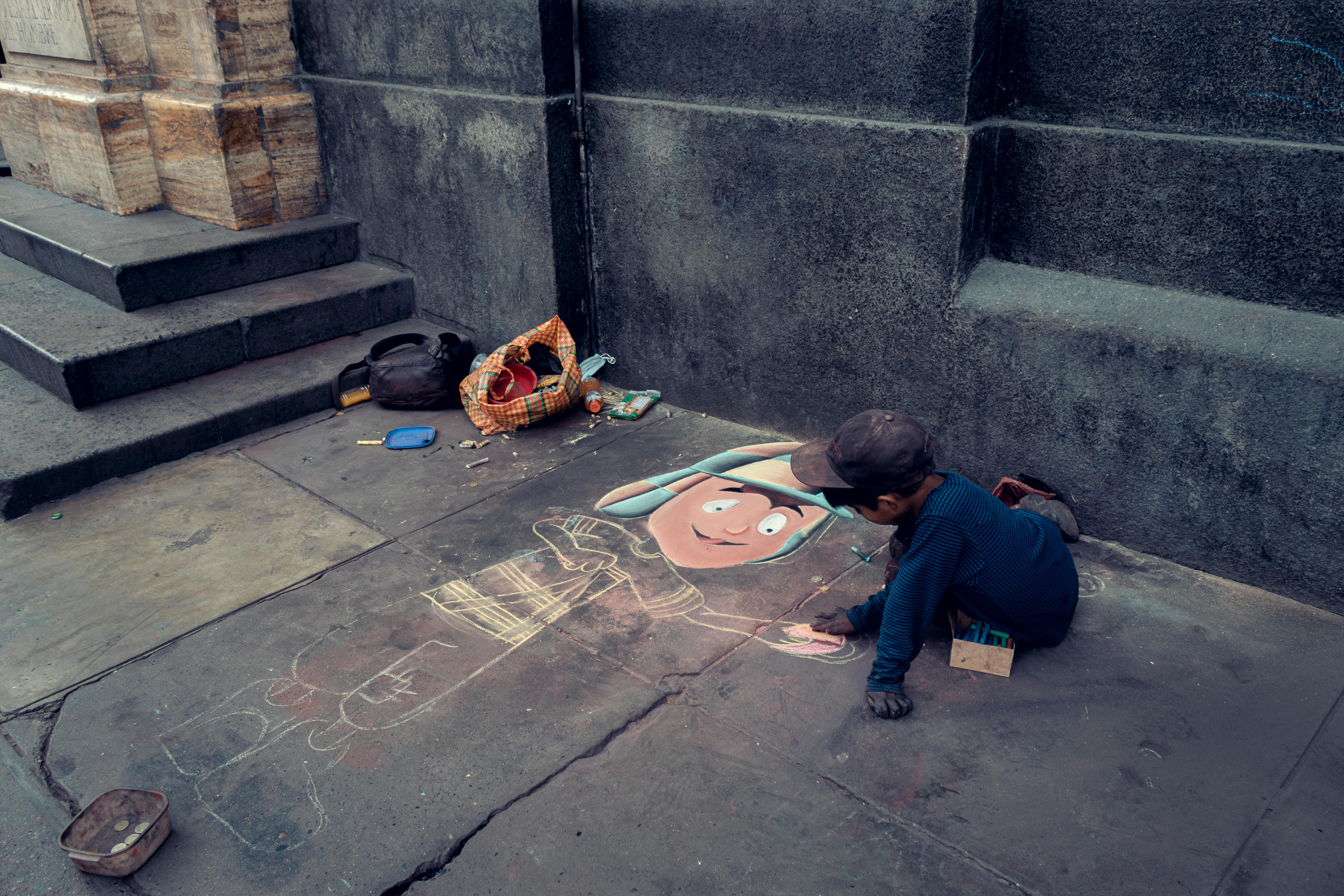 A young boy creates vibrant pavement art on a city sidewalk, capturing urban creativity.