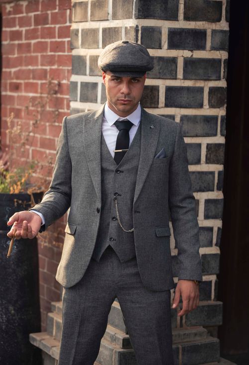 Free Portrait of a confident man in vintage attire holding a cigar outside a brick building. Stock Photo