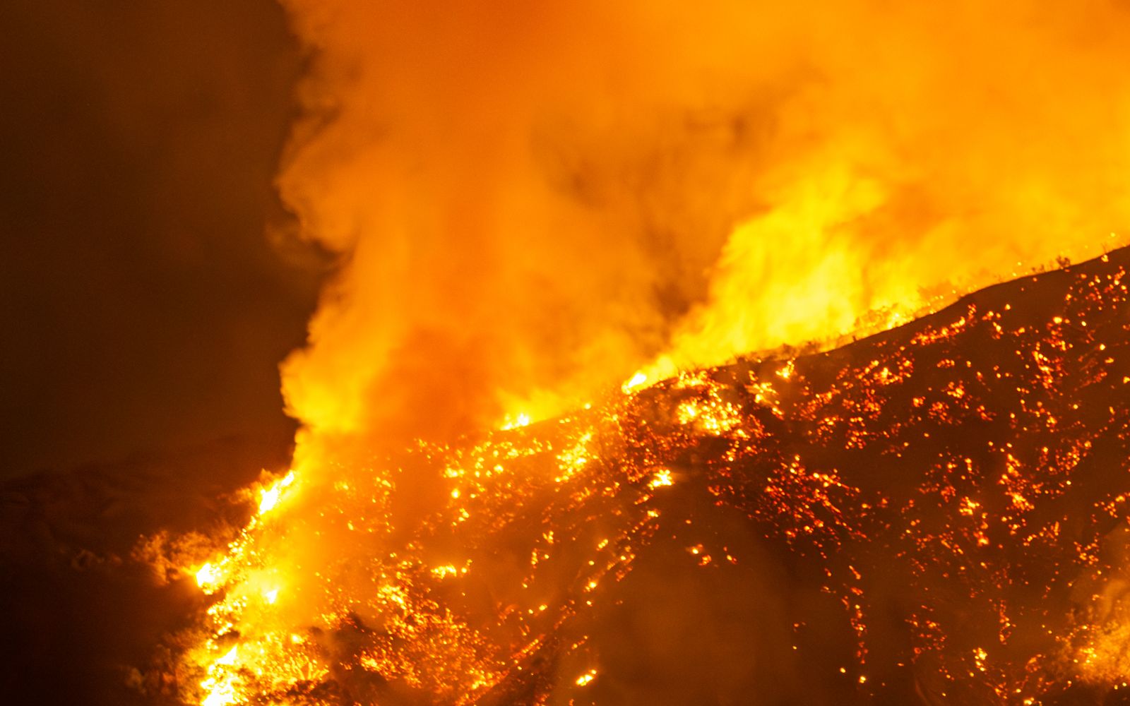 A wildfire burns intensely on a hillside at night in California