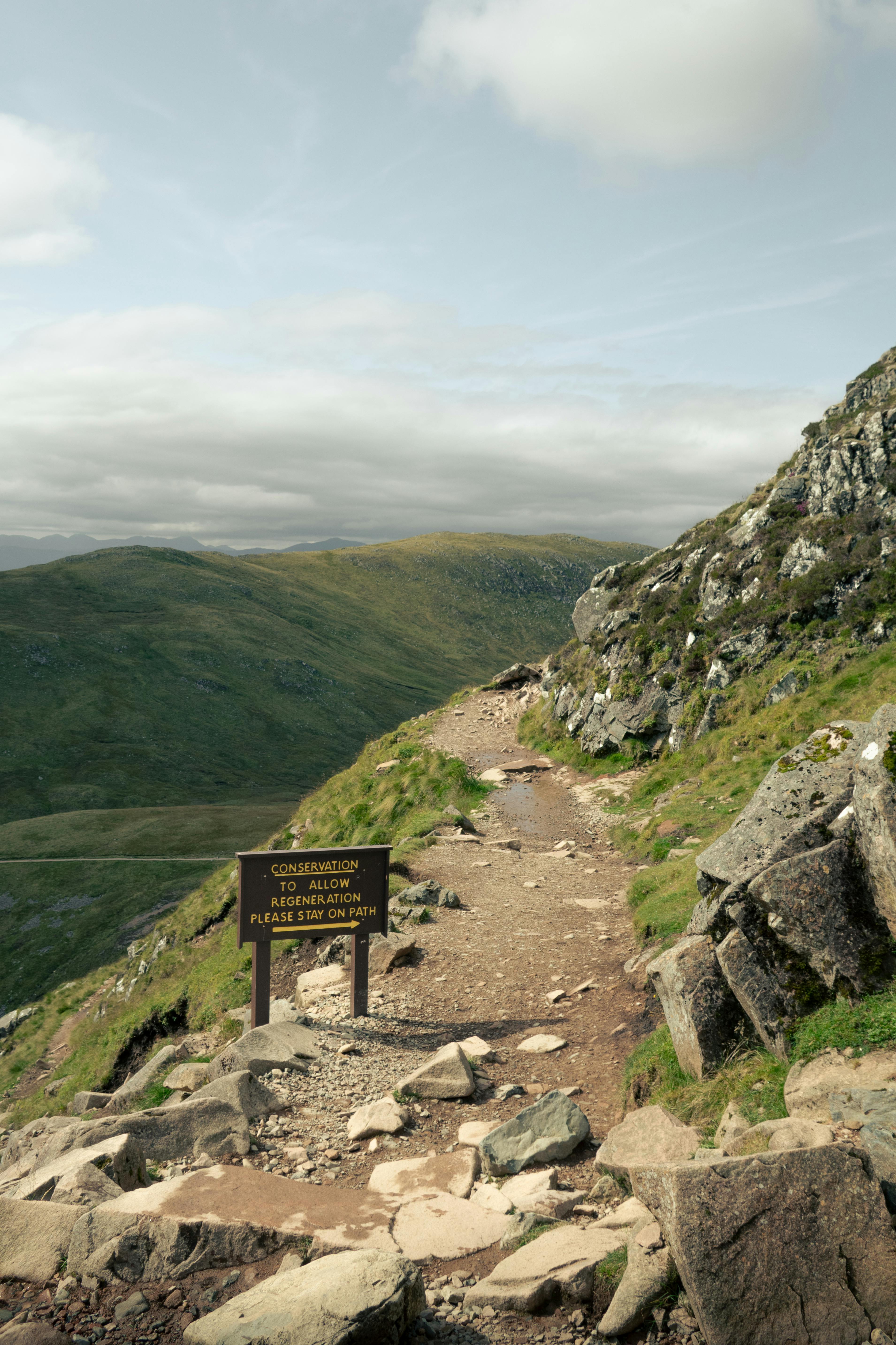 Rugged mountain trail surrounded by rocks and greenery under a cloudy sky.