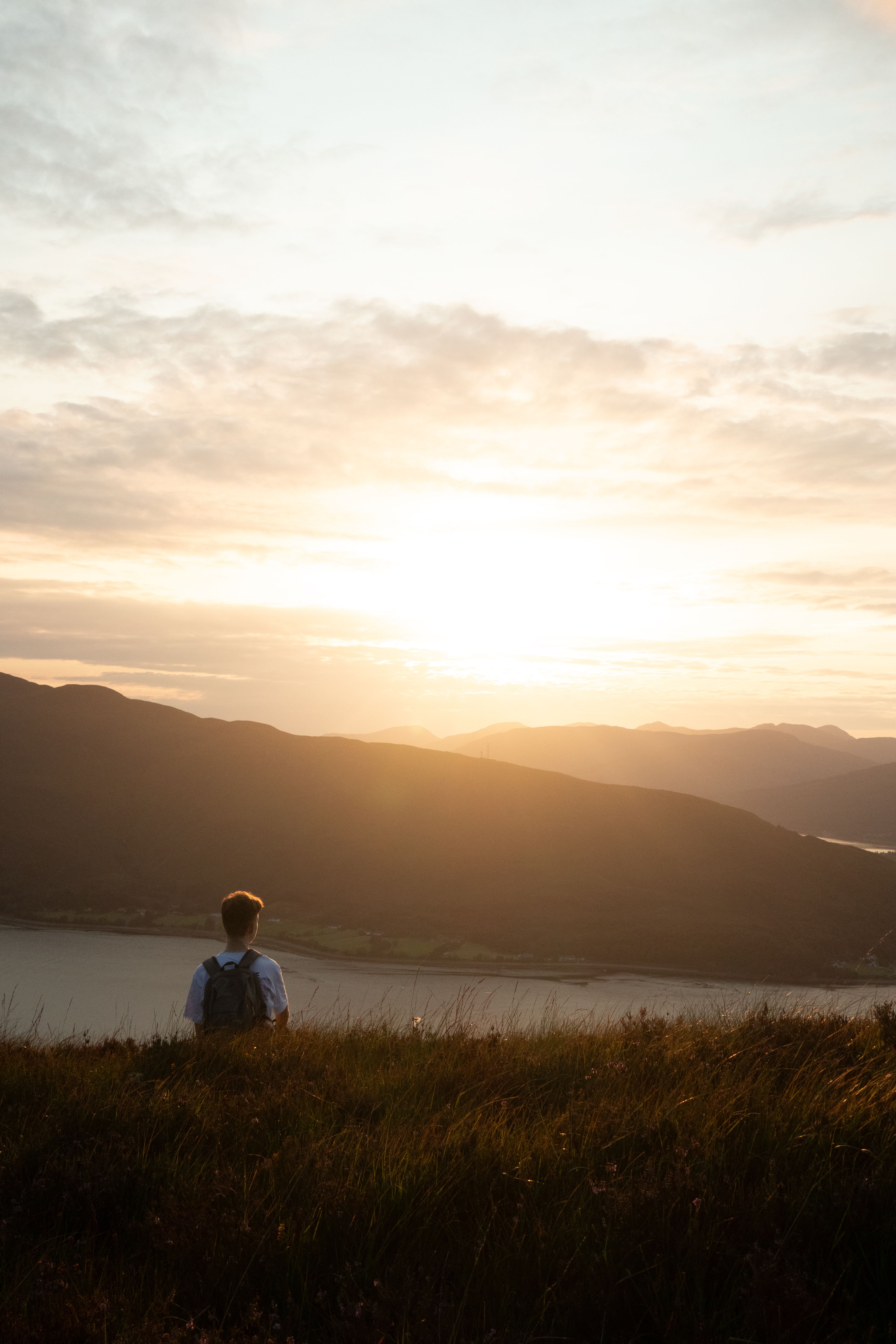 A person sitting on a hill looking at the sunset · Free Stock Photo