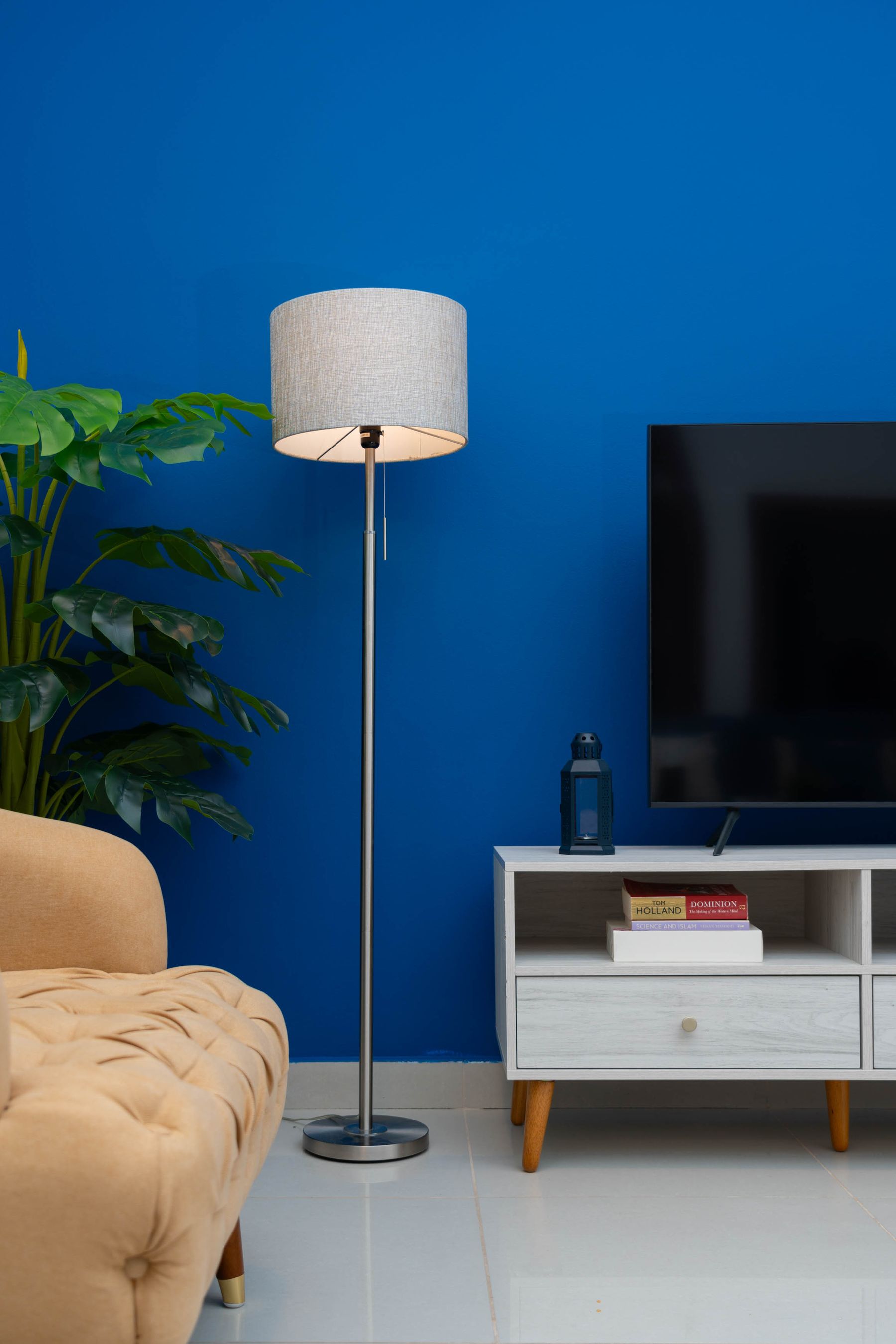 Vivid cobalt blue living room wall behind a black television, pale media console, floor lamp, plant and beige seating edge