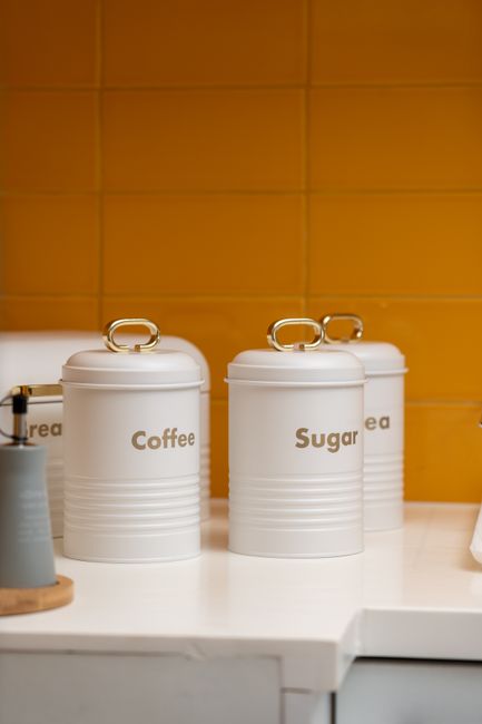 Elegant white kitchen canisters labeled for coffee and sugar, against a vibrant yellow backsplash. - Importance of Proper Storage for Dry Fruits