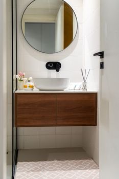 Stylish bathroom featuring a round mirror, vessel sink, and wooden cabinet. Ideal for modern interior design themes.
