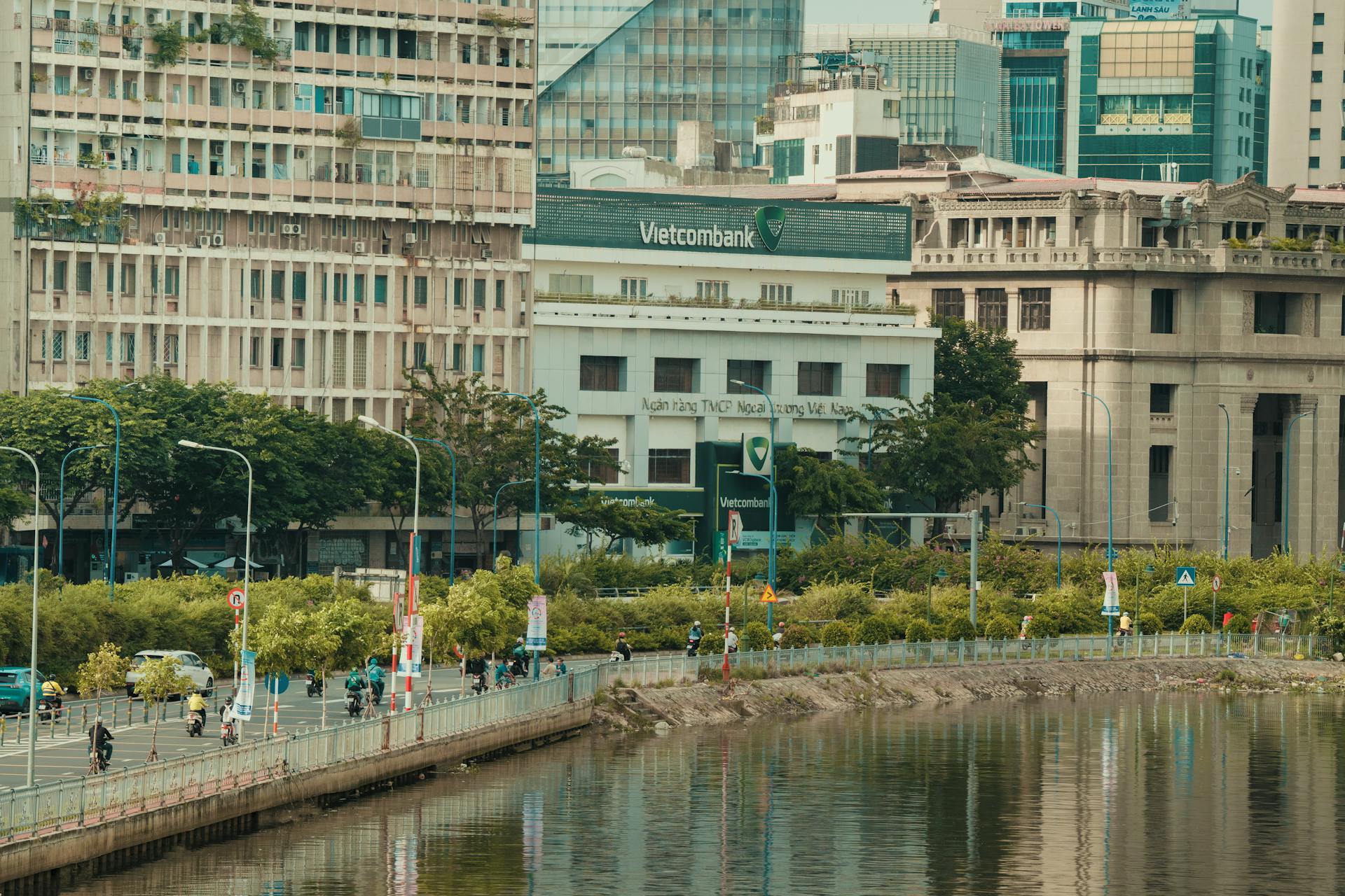 Street scene featuring Vietcombank building along a riverside in urban Ho Chi Minh City, Vietnam.