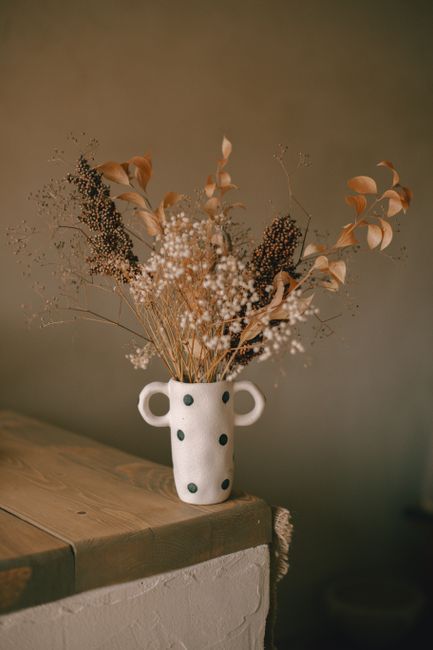 A charming still life featuring a ceramic vase with dried flowers in a warm autumn setting.