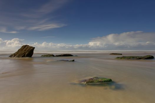 Tranquil seascape at Watergate Beach, England featuring rocks and a calm sea under a blue sky.
