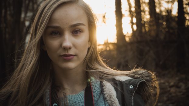 Close-up portrait of a young woman in a forest during golden hour, showcasing natural beauty.