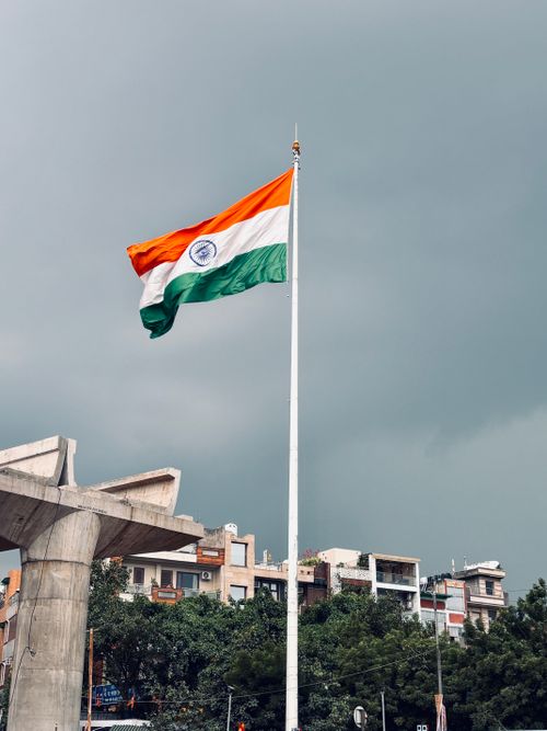 Free Indian flag waving in a cityscape with overcast skies, showcasing national pride. Stock Photo