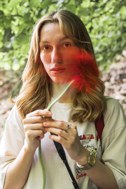A young woman holds a flower, enjoying a peaceful day outdoors in summer.