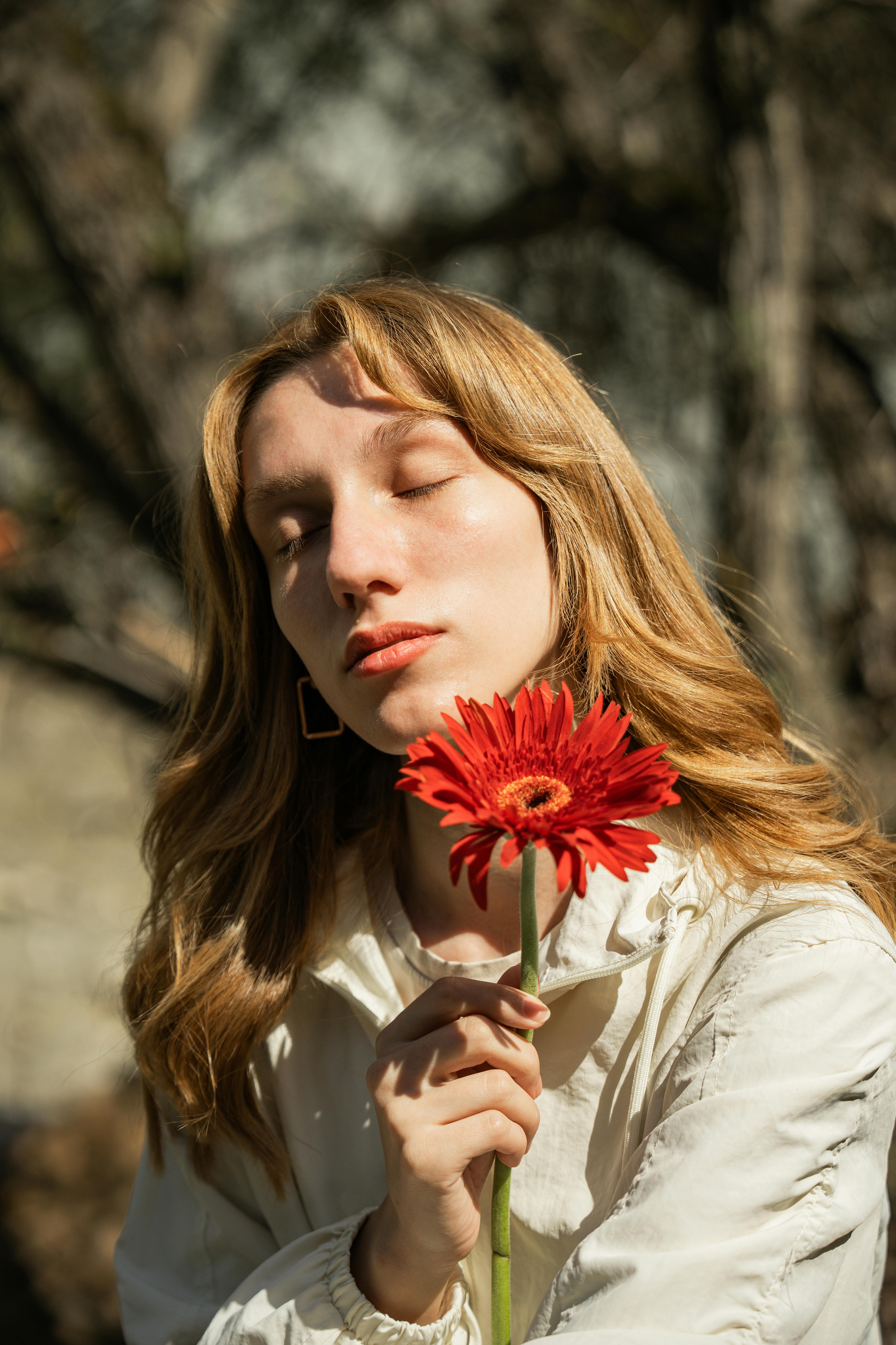A serene portrait of a young woman with a red flower outdoors.