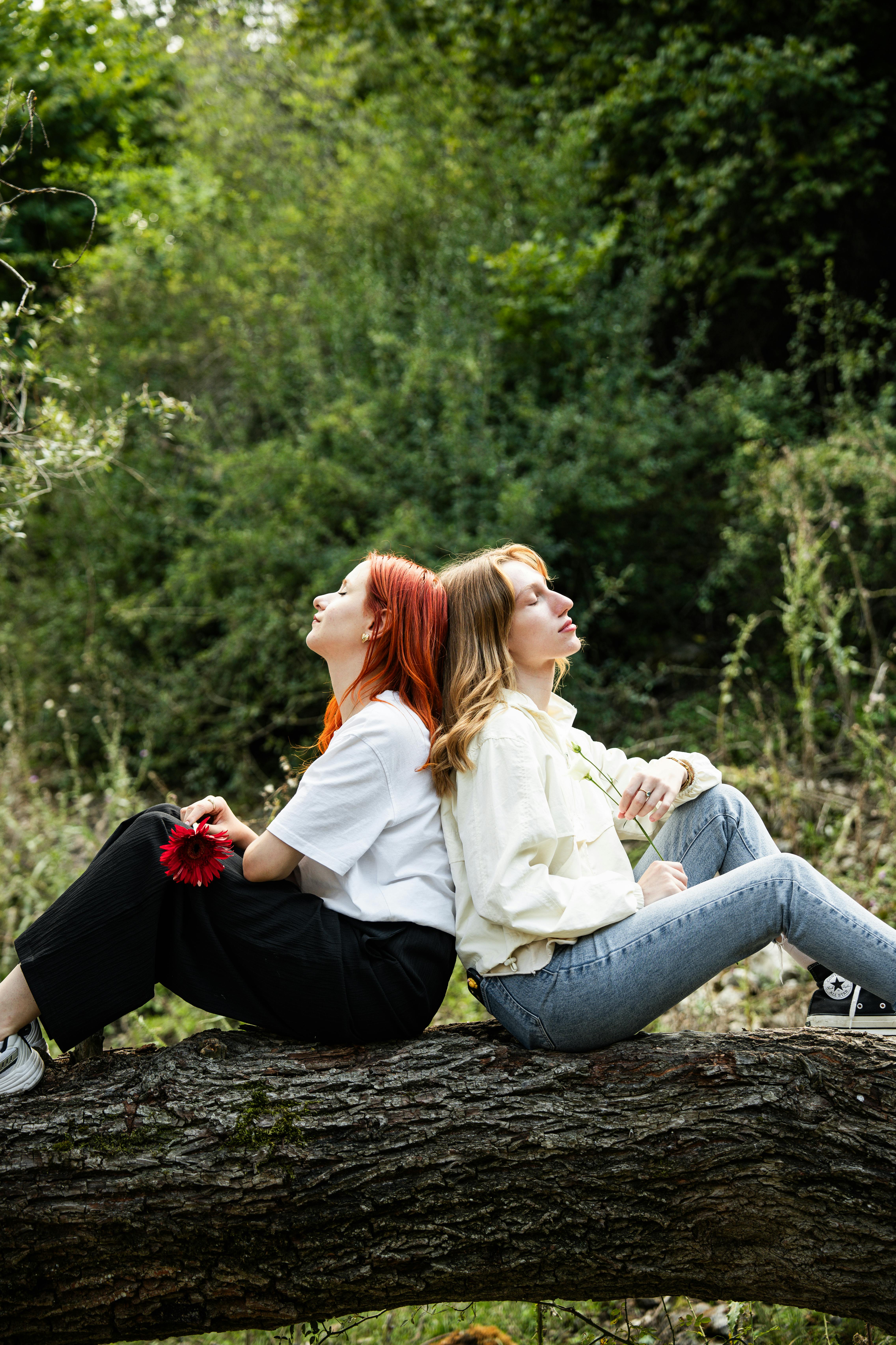 Two women sitting on a fallen tree enjoying a serene moment in nature.