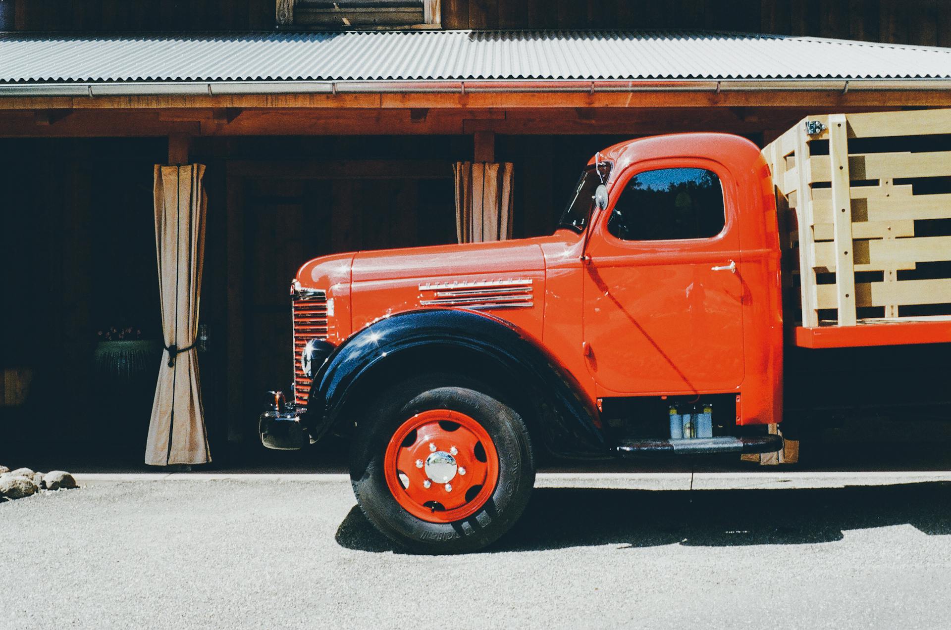 A vibrant red vintage truck parked outside a rustic building, showcasing classic design elements.