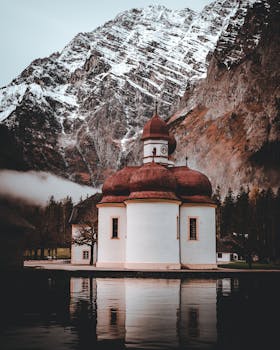 白雪皑皑的山峰下，一个平静的山湖依偎在迷人的小教堂旁