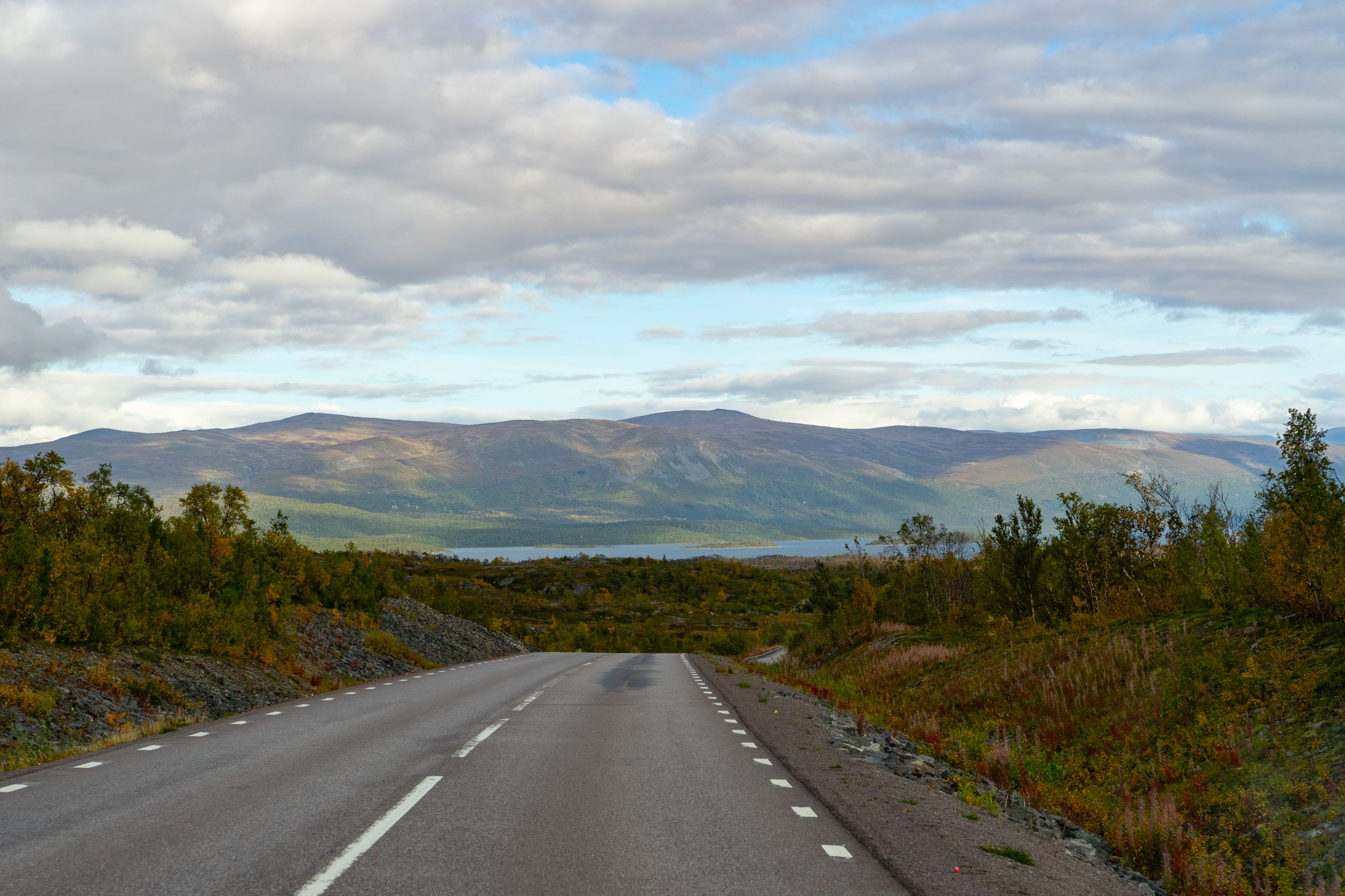 A serene road through the picturesque landscape of Kiruna, Sweden, with distant mountains.