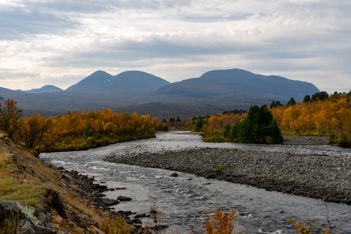 Free Autumn landscape of a serene river in Kiruna, Sweden, surrounded by fall foliage and mountains. Stock Photo