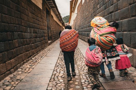 Family in colorful ponchos walking down a historic alley, showcasing South American culture.