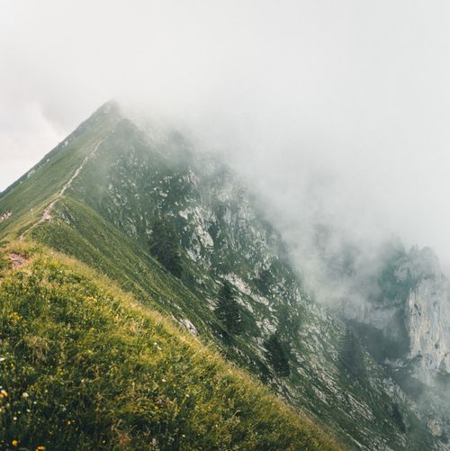 Free A breathtaking view of a fog-covered mountain peak with lush green hills and rocky terrain. Stock Photo