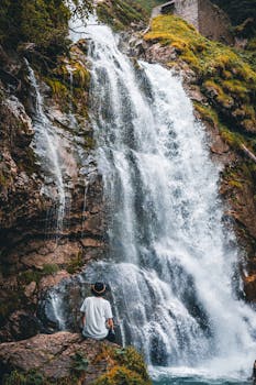 一位戴着帽子的人，坐在宁静的瀑布旁，四周郁郁葱葱，捕捉着自然之美的本质