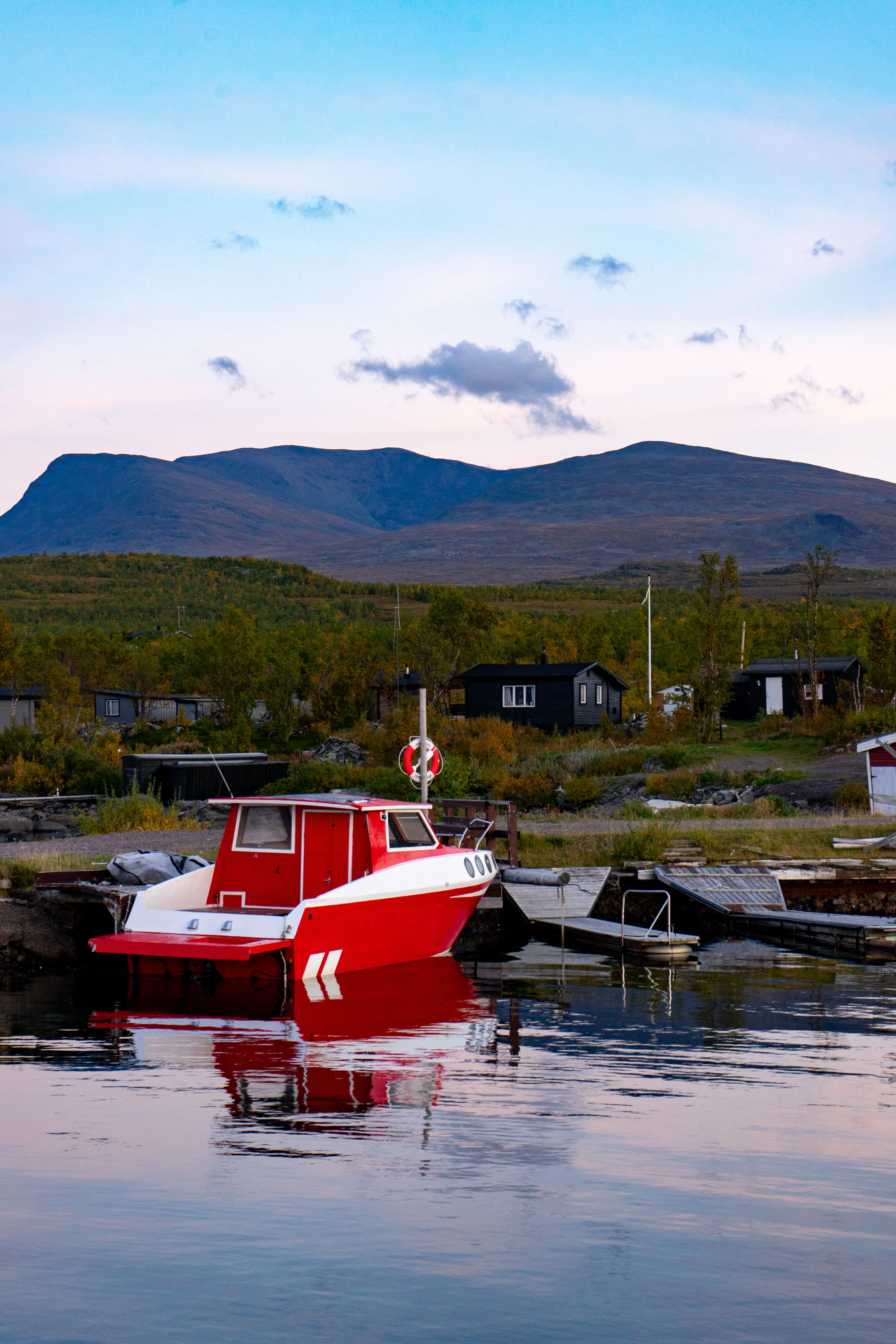 Serene view of a red motorboat moored in Kiruna's harbor with scenic mountains in the background.