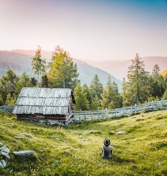 日落时分，群山和树木环绕的小屋，映衬着宁静的乡村景色