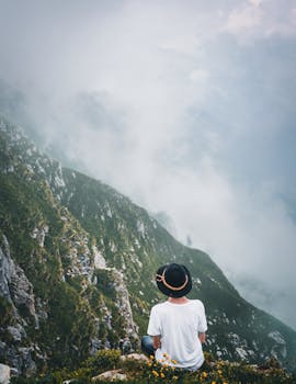 一个穿着休闲服装的人，孤独地坐在雾蒙蒙山脉的悬崖上