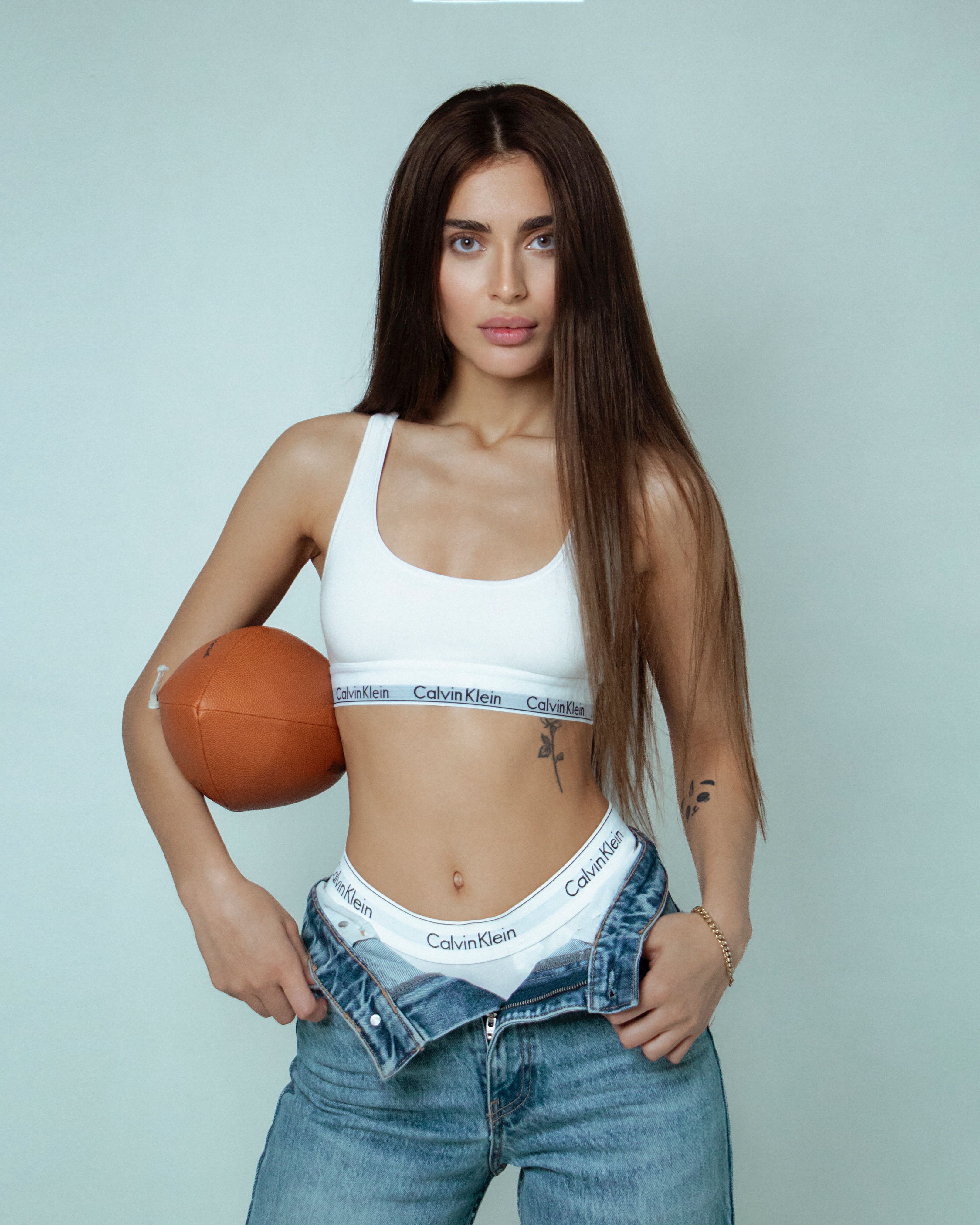 Portrait of a young woman in Calvin Klein sports bra with an American football, showcasing sporty fashion style.