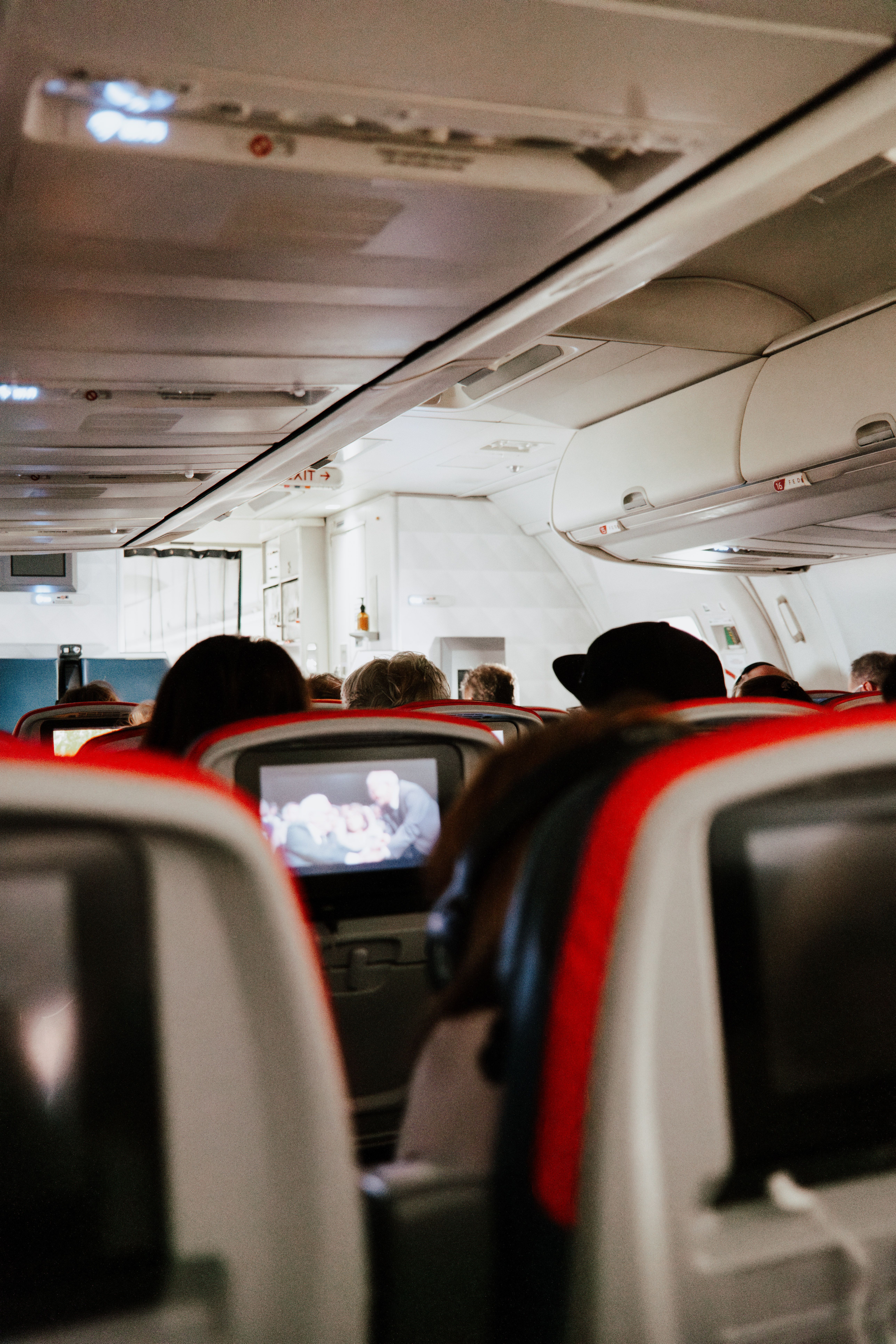 View of passengers seated in an airplane, watching in-flight entertainment.