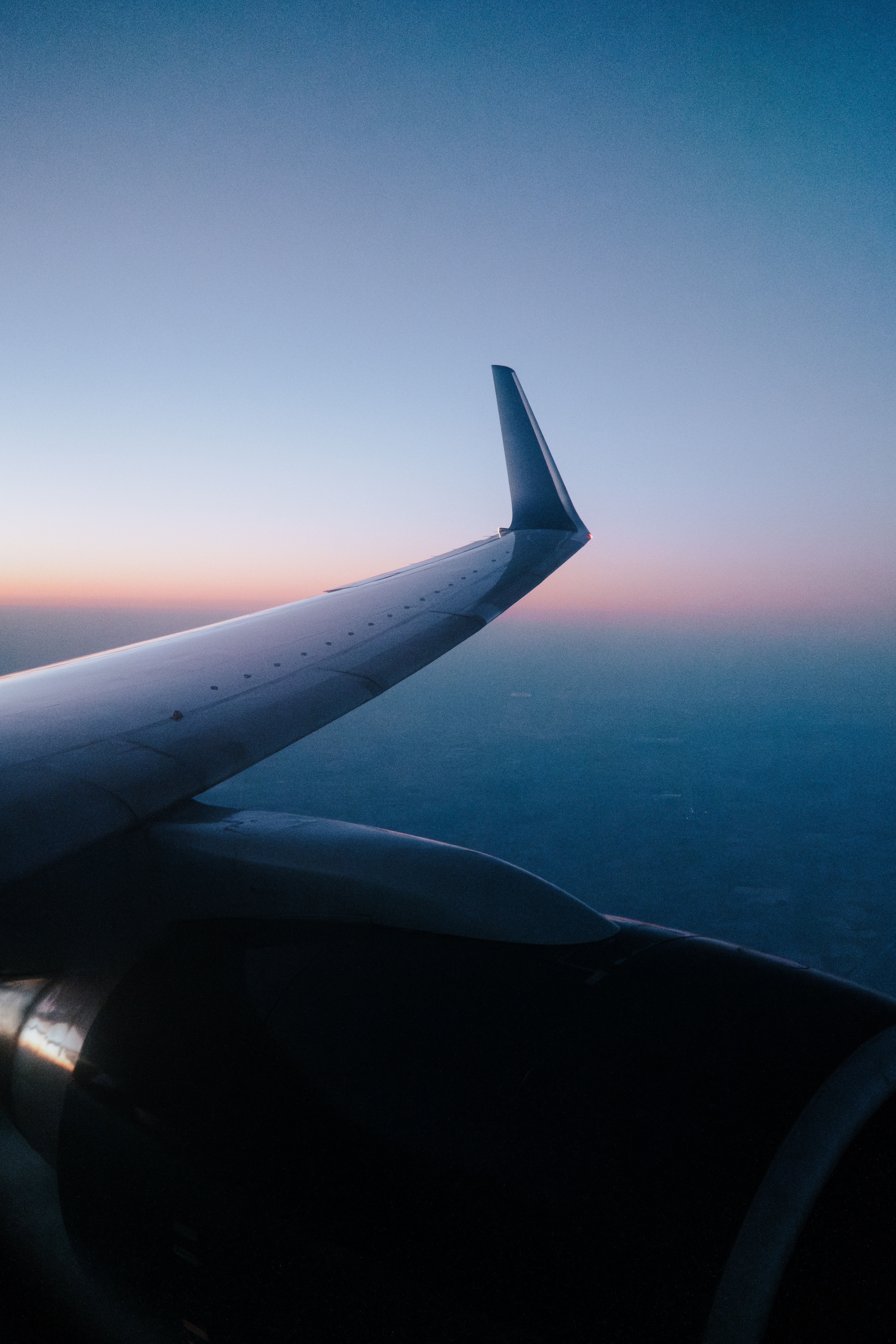View of an aircraft wing above a cloud layer at dusk, the sky fading from amber to deep blue