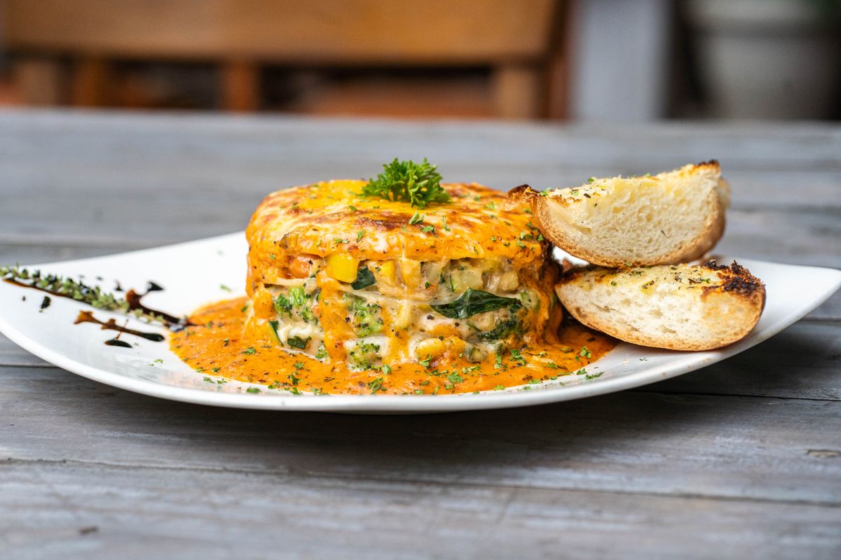 Tall layered vegetable lasagna stack in orange pepper sauce with toasted garlic bread