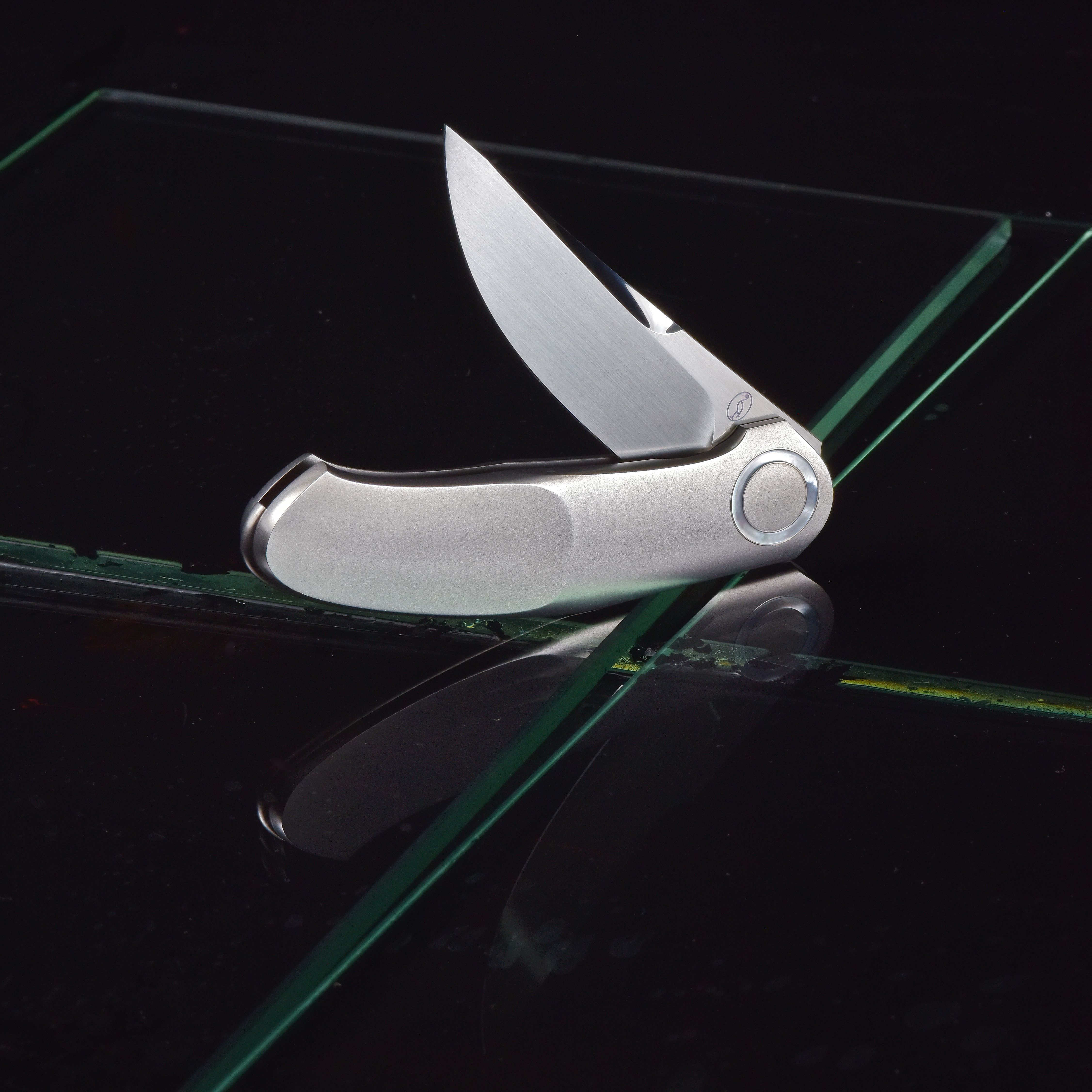 Elegant stainless steel folding pocket knife on reflective glass surface.