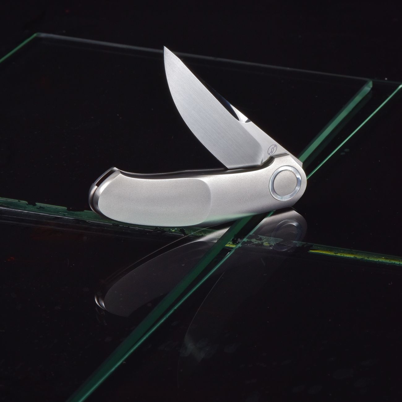 Elegant stainless steel folding pocket knife on reflective glass surface.