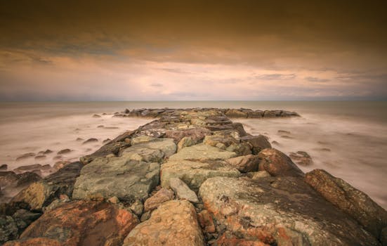 Rocky shoreline leading into the ocean under a dramatic sunset sky.